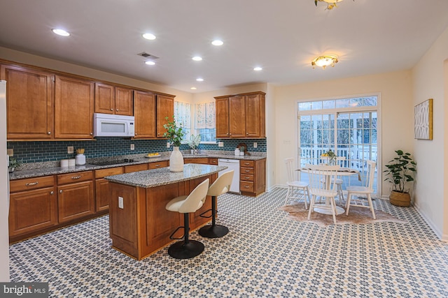 kitchen featuring a kitchen bar, a center island, white appliances, light stone counters, and sink