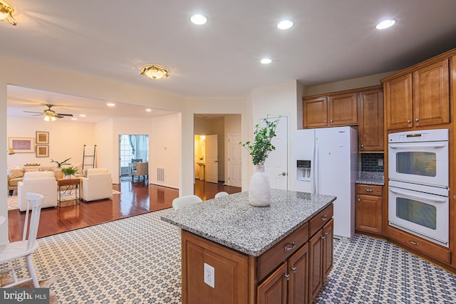 kitchen featuring light stone countertops, white appliances, a center island, decorative backsplash, and ceiling fan