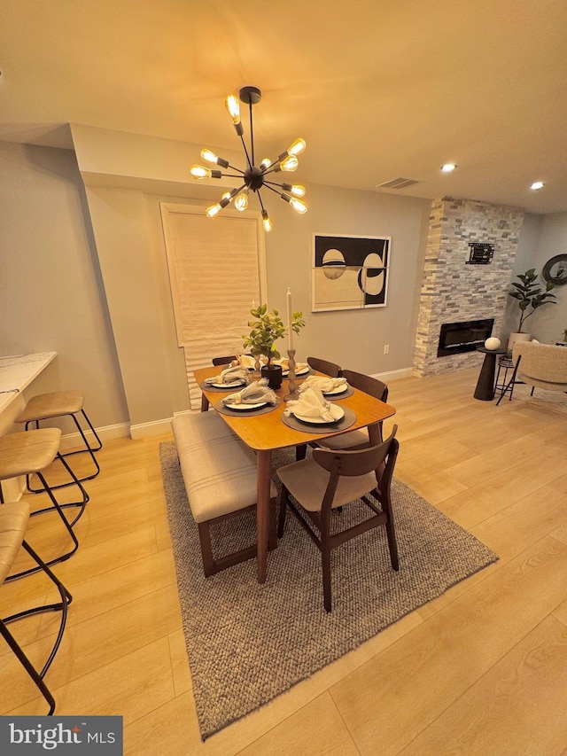 dining space featuring light hardwood / wood-style flooring, an inviting chandelier, and a stone fireplace