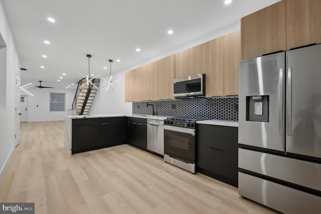 kitchen featuring pendant lighting, ceiling fan, light wood-type flooring, kitchen peninsula, and stainless steel appliances