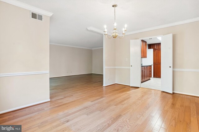 spare room with ornamental molding, light wood-type flooring, and an inviting chandelier