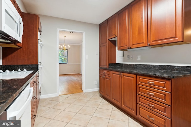 kitchen featuring light tile patterned flooring, dark stone counters, white appliances, and a notable chandelier