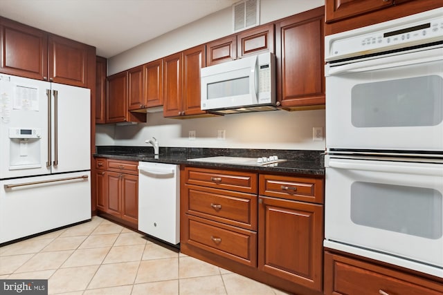 kitchen with sink, light tile patterned flooring, dark stone counters, and white appliances