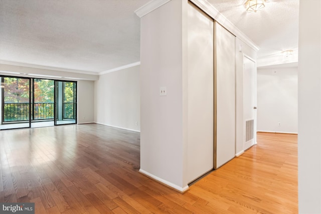 hallway with crown molding, a textured ceiling, and light wood-type flooring