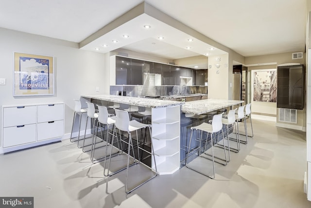 kitchen with a kitchen bar, backsplash, light stone counters, sink, and white cabinets