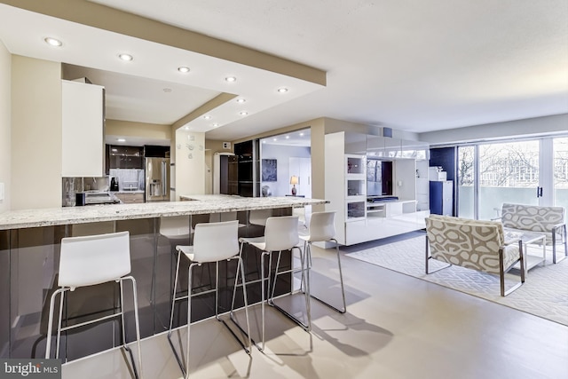 kitchen featuring white cabinetry, light stone countertops, stainless steel fridge with ice dispenser, kitchen peninsula, and a breakfast bar area