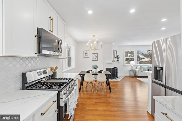 kitchen with light stone countertops, decorative backsplash, stainless steel appliances, pendant lighting, and white cabinets