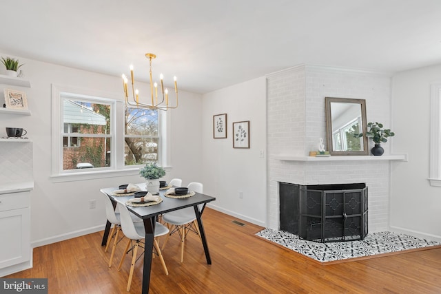 dining area with light wood-type flooring, a brick fireplace, and a notable chandelier