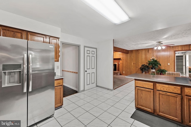 kitchen with ceiling fan, a brick fireplace, stainless steel fridge, a textured ceiling, and wooden walls