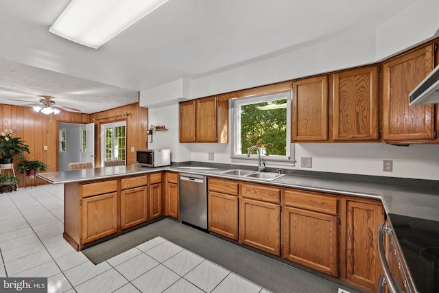 kitchen with kitchen peninsula, stainless steel appliances, ceiling fan, sink, and wood walls