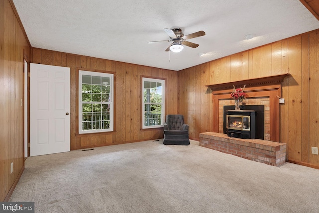 unfurnished living room featuring carpet, ceiling fan, a wood stove, and a textured ceiling