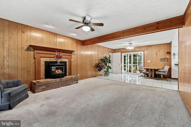 carpeted living room with ceiling fan, beam ceiling, a textured ceiling, and wooden walls