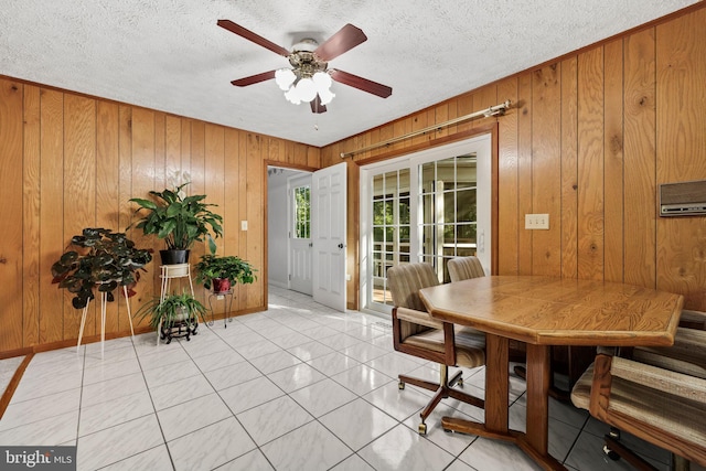 dining area featuring ceiling fan, light tile patterned floors, a textured ceiling, and wooden walls