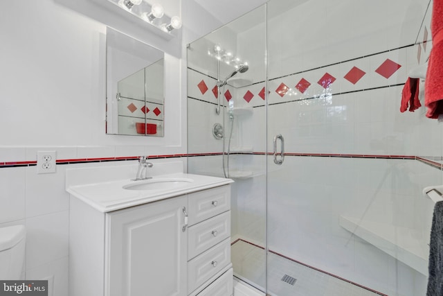 bathroom with vanity, toilet, a shower with door, and tile walls