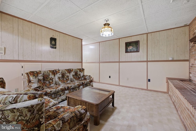 living room featuring a drop ceiling and wooden walls