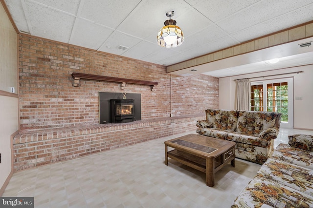 living room with a paneled ceiling, brick wall, and a wood stove