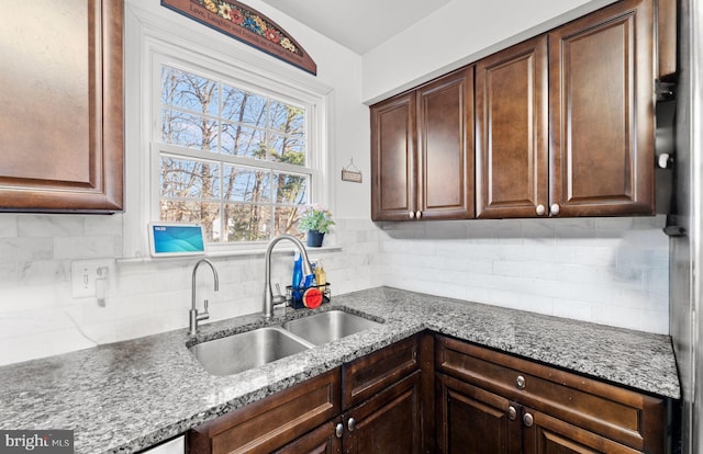 kitchen featuring decorative backsplash, sink, light stone counters, and dark brown cabinets