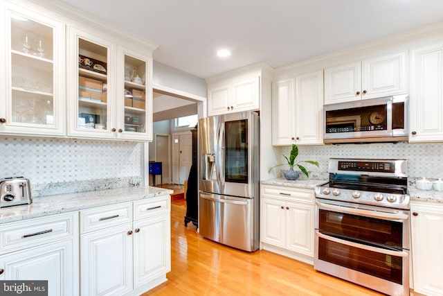 kitchen with backsplash, stainless steel appliances, light hardwood / wood-style floors, and white cabinets