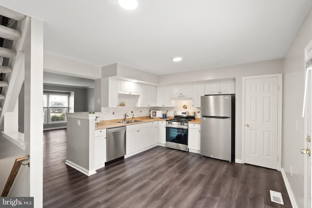 kitchen with appliances with stainless steel finishes, white cabinets, sink, kitchen peninsula, and dark wood-type flooring