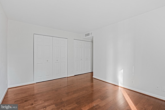 unfurnished bedroom with two closets and hardwood / wood-style flooring