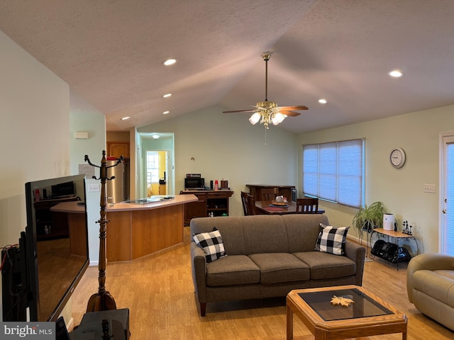 living room with lofted ceiling, ceiling fan, light wood-type flooring, and a textured ceiling