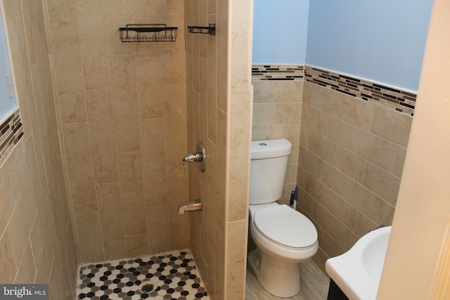 bathroom with a tile shower, toilet, and tile walls