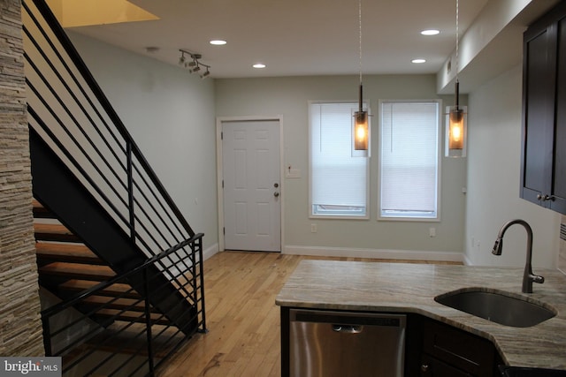 kitchen featuring light wood-type flooring, light stone counters, stainless steel dishwasher, sink, and pendant lighting