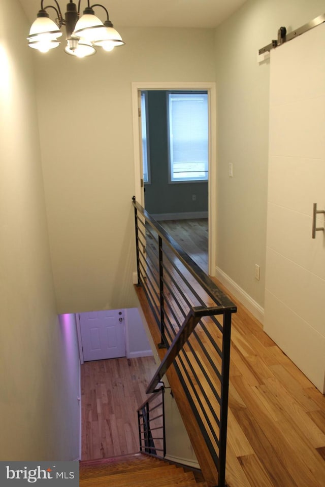 staircase featuring a barn door, wood-type flooring, and a notable chandelier