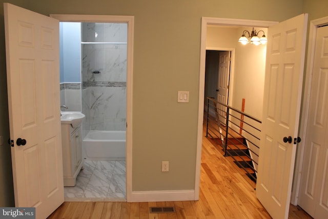 bathroom with vanity, tiled shower / bath, wood-type flooring, and an inviting chandelier