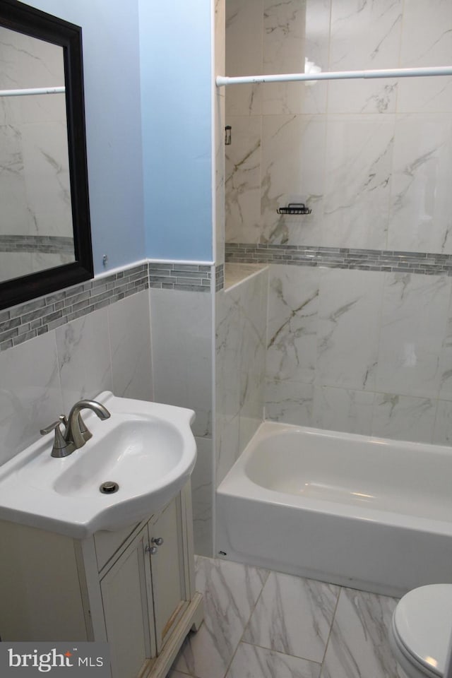 full bathroom with vanity, tiled shower / bath combo, toilet, and tile walls