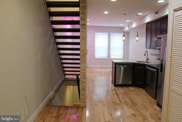 kitchen with kitchen peninsula, appliances with stainless steel finishes, light wood-type flooring, sink, and hanging light fixtures