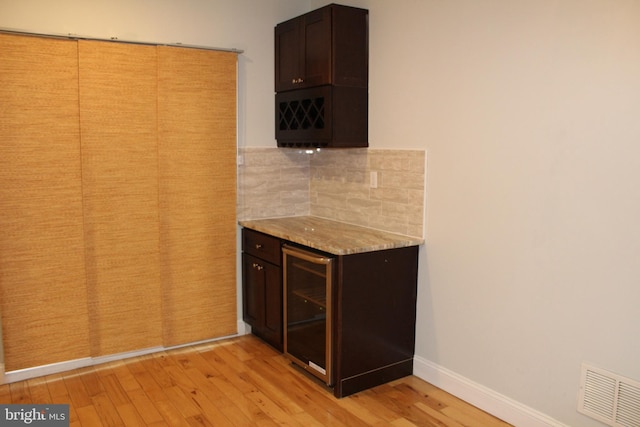 kitchen featuring dark brown cabinetry, light hardwood / wood-style floors, beverage cooler, and backsplash