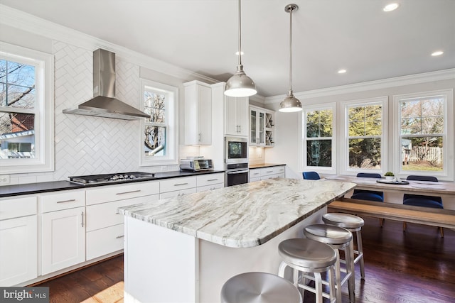 kitchen with stainless steel appliances, wall chimney range hood, a kitchen bar, and crown molding