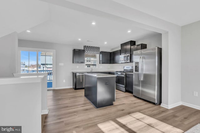 kitchen featuring a kitchen island, light stone counters, stainless steel appliances, and light hardwood / wood-style flooring