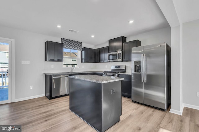 kitchen featuring light stone countertops, appliances with stainless steel finishes, sink, light hardwood / wood-style flooring, and a center island