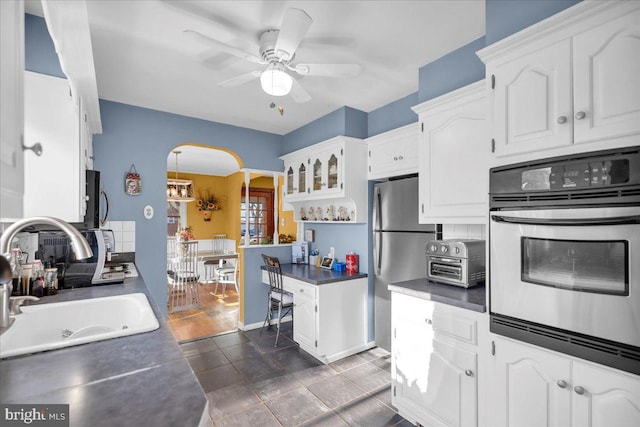 kitchen with stainless steel fridge, wall oven, ceiling fan, sink, and white cabinets