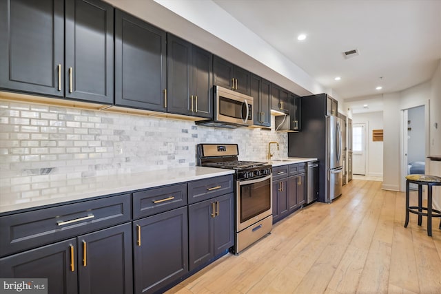 kitchen with appliances with stainless steel finishes, backsplash, light hardwood / wood-style flooring, and sink