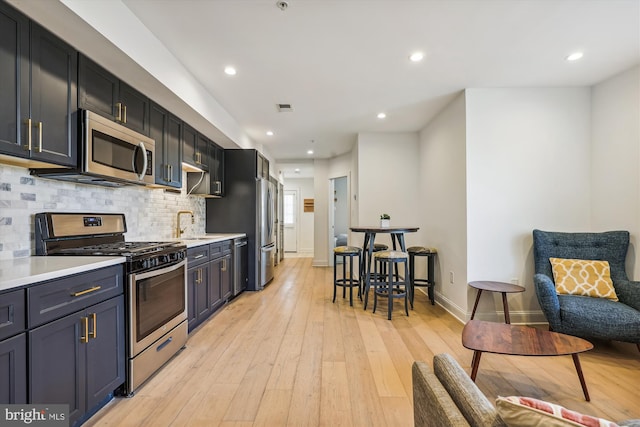 kitchen featuring tasteful backsplash, sink, light wood-type flooring, and appliances with stainless steel finishes