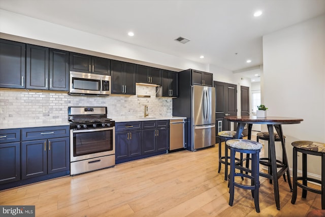 kitchen with blue cabinetry, sink, stainless steel appliances, decorative backsplash, and light wood-type flooring