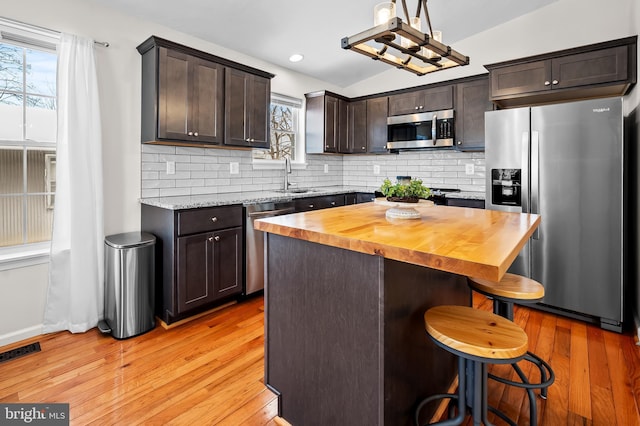 kitchen featuring wood counters, a breakfast bar area, appliances with stainless steel finishes, a center island, and sink