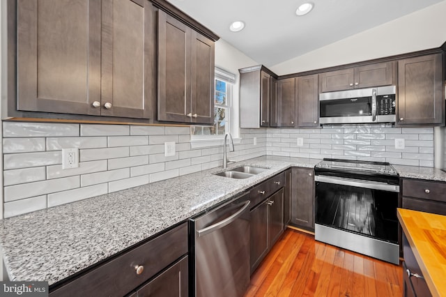 kitchen featuring vaulted ceiling, wood counters, stainless steel appliances, sink, and light wood-type flooring