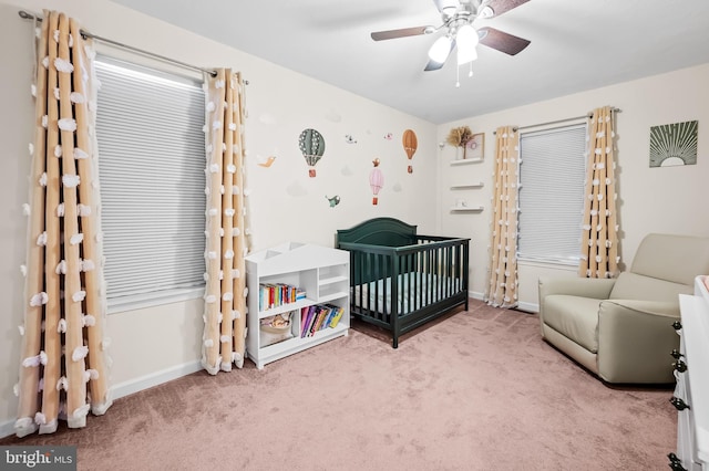 carpeted bedroom with ceiling fan and a nursery area