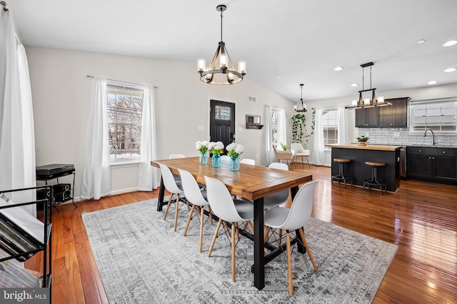 dining space with sink, lofted ceiling, a notable chandelier, and light wood-type flooring