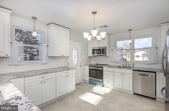 kitchen with light stone countertops, appliances with stainless steel finishes, pendant lighting, and white cabinetry