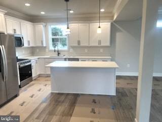 kitchen featuring wood finished floors, a center island, stainless steel appliances, light countertops, and white cabinetry