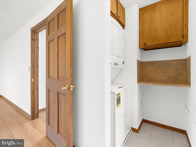 clothes washing area with cabinets and stacked washing maching and dryer