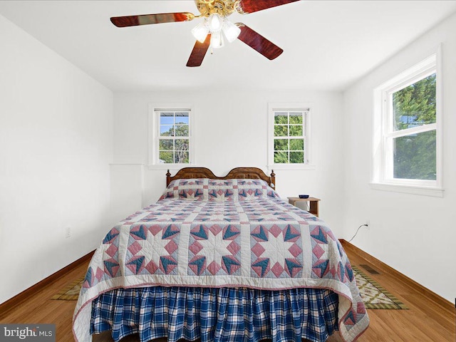 bedroom with multiple windows, wood-type flooring, and ceiling fan