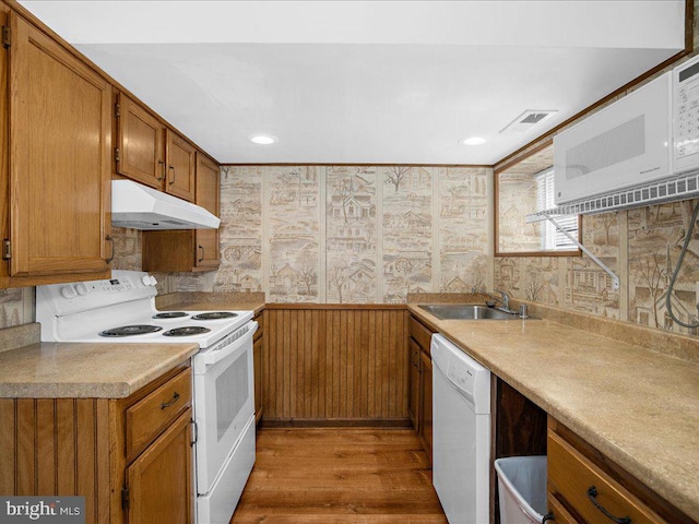 kitchen featuring wooden walls, sink, white appliances, and hardwood / wood-style flooring