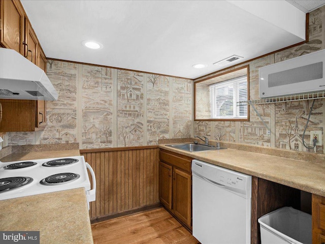 kitchen with wood walls, white appliances, sink, ornamental molding, and light hardwood / wood-style floors