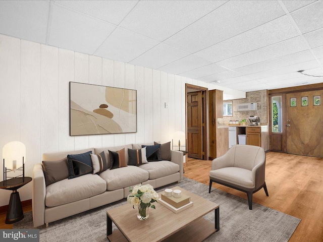 living room with light wood-type flooring, a drop ceiling, and wooden walls